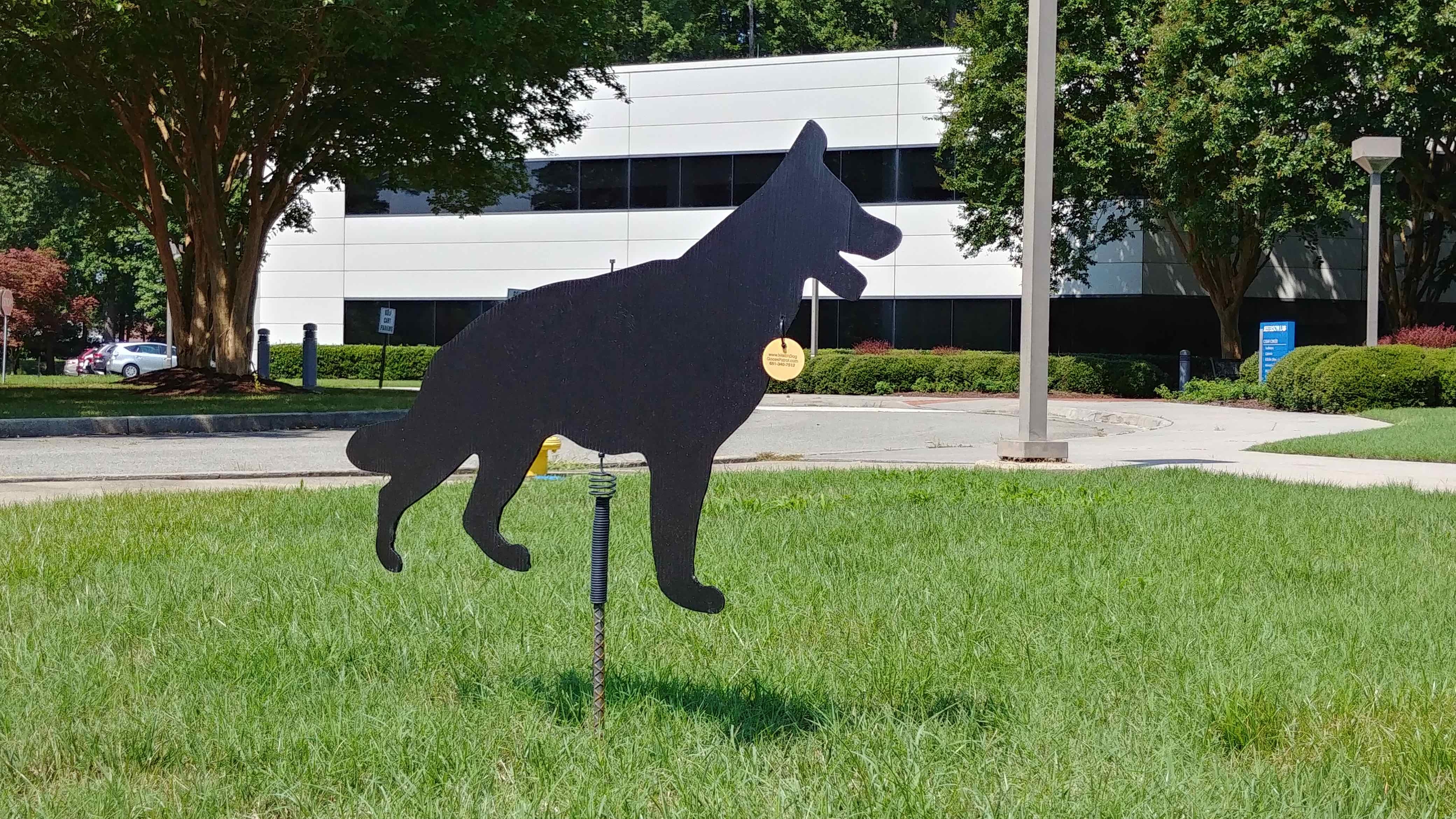 Black corrugated plastic dog cutout attached to a stake embedded in the front lawn of the CEBAF Center Bldg. on the Jefferson Lab campus.