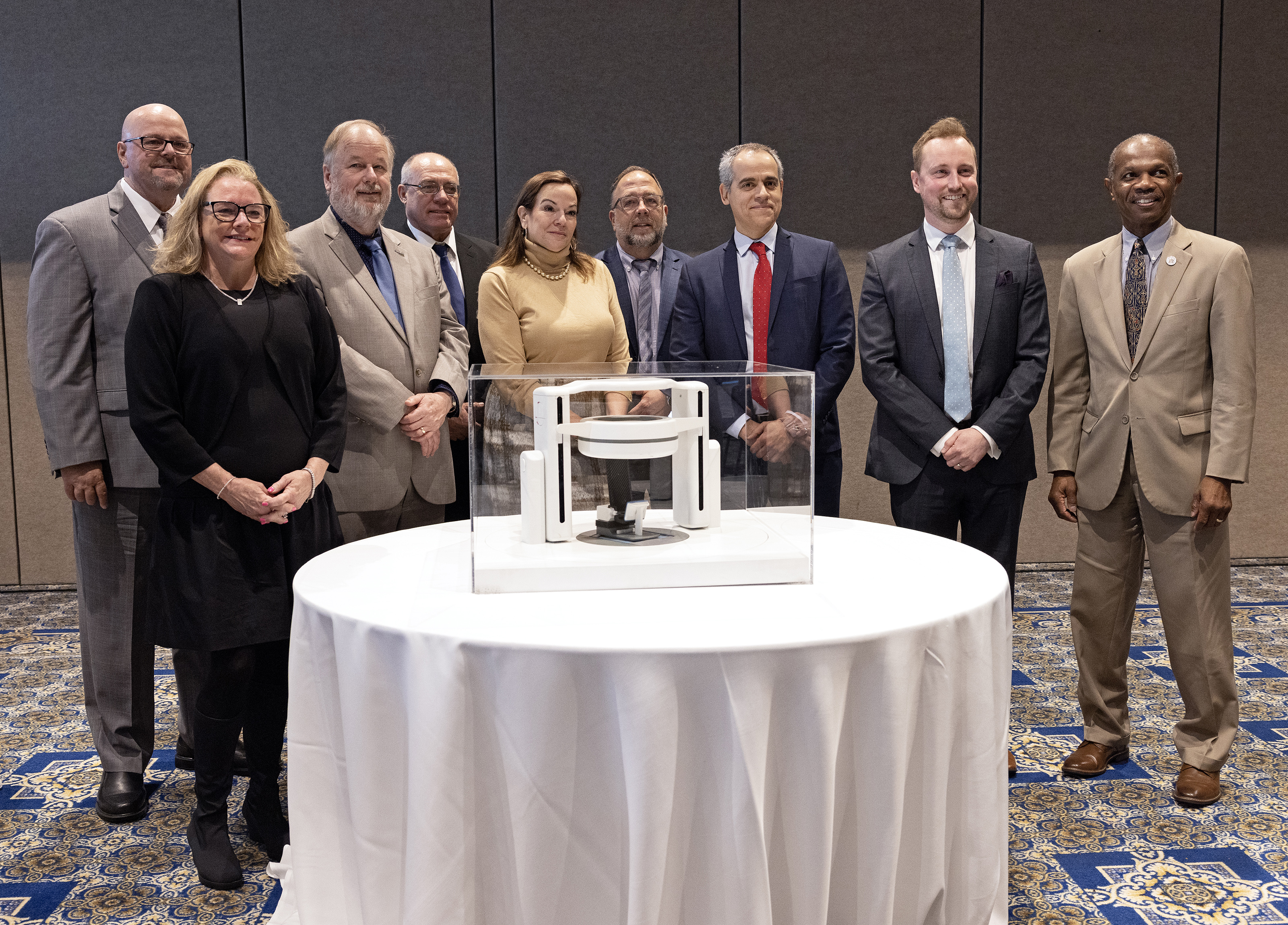 Members of the Hampton University Proton Therapy Institute (HUPTI), Leo Cancer Care, Jefferson Lab, and the City of Hampton pose for a photograph next to the upright radiation therapy prototype during a press announcement held at Hampton University