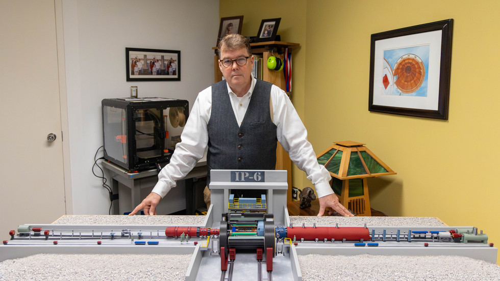 A man poses with a table-size, 3D-printed model of a section of the Electron Ion Collider.