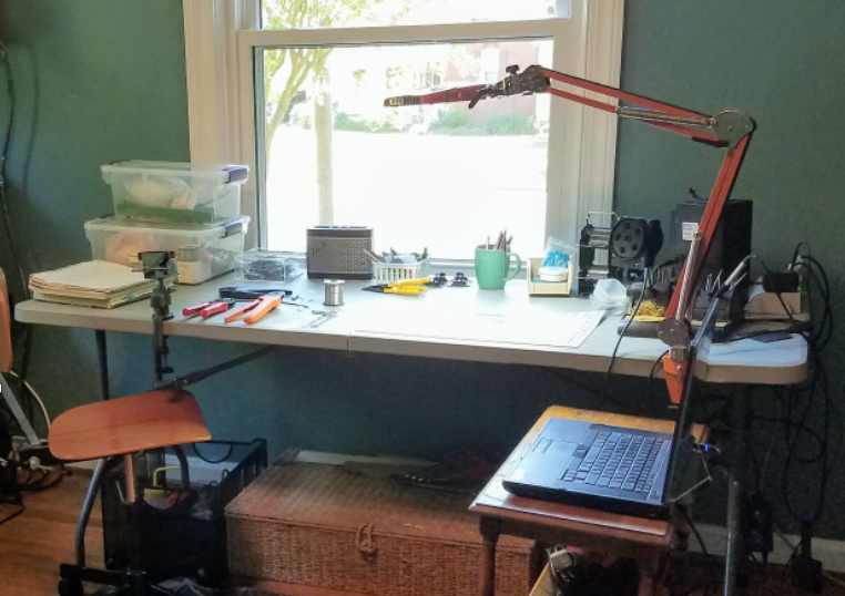 A home-based workspace with a table, chair against a window.