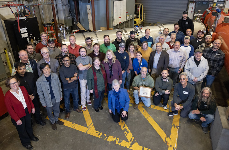 یک عکس گروهی از همکاران آزمایشگاه جفرسون بر روی ماژول سرمای SNS PPU CM-08 که به منبع نوترون Spallation در آزمایشگاه ملی Oak Ridge تحویل داده شد.