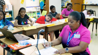  A classroom of students watch a female teacher provide instruction. 