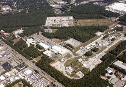 An overhead view of Jefferson Lab. To the right is the racetrack outline of the lab's  accelerator, while at the bottom right the lab's experimental halls are visible as three round mounds. The two white buildings (center) are part of the TEDF. The white building to the left is the EEL building.