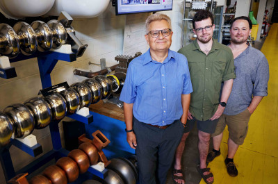Alex Bogacz, Alex Coxe and Ryan Bodenstein (l-r) stand next to a display of particle accelerator components.