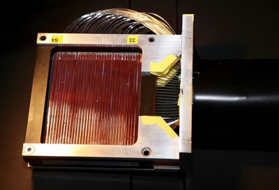 Square detector head with numerous clear glass fibers across the top surface and out the side.